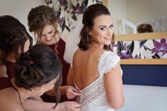 Becca's bridal party helping her fasten her dress before her wedding at Grinkle Park