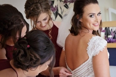 Becca's bridal party helping her fasten her dress before her wedding at Grinkle Park