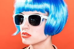 Blue hair, sunglasses, orange lips and orange background.  Editorial makeup.